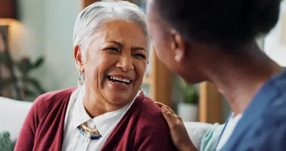 Dementia care worker sharing a happy conversation with an older woman during a home visit.