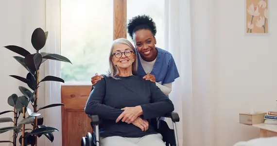 Dementia care worker supporting an older woman seated in a wheelchair at home.