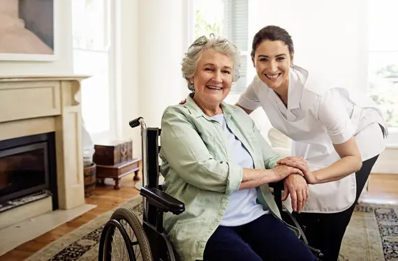 Dementia care worker supporting an older woman seated in a wheelchair at home.