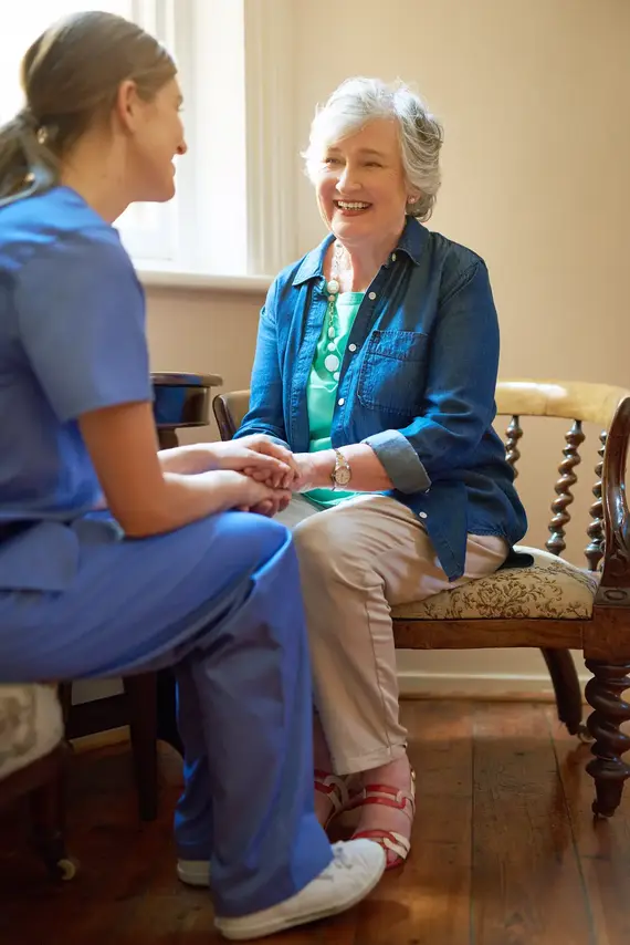 Dementia care worker holding hands and talking with an older woman in her home.