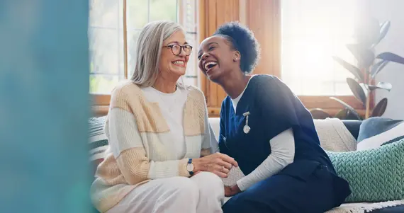 Dementia care worker laughing with an older woman while providing companionship at home.