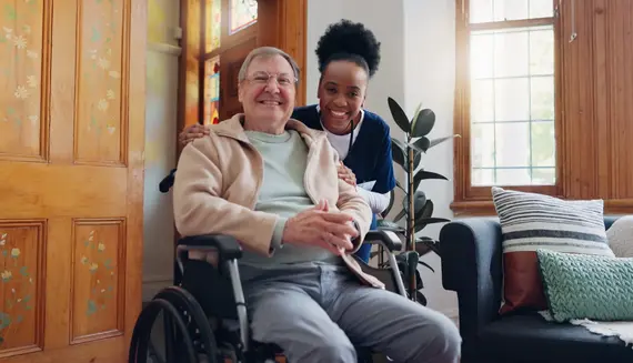 Dementia care worker supporting an older man seated in a wheelchair in his home.