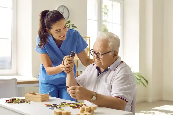 Dementia care worker helping an older man complete a puzzle activity at home.