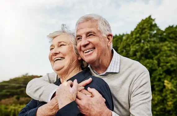 A cheerful elderly couple embrace outdoors, reflecting the joy and independence that quality senior care at home can provide.